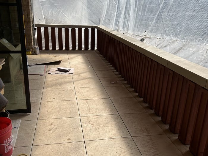 Balcony wrapped in protective mesh, balusters and stone handrail caps staged.