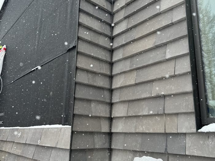 Interior corner where the cladding meets black metal trim, panels going up in the snow.