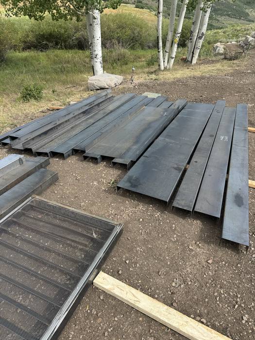 Raw steel beams and plates staged on the ground — start of the steel package.