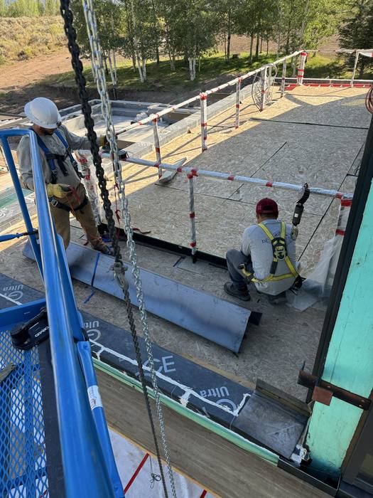 Crew on a lift maneuvering a large steel plate into position.