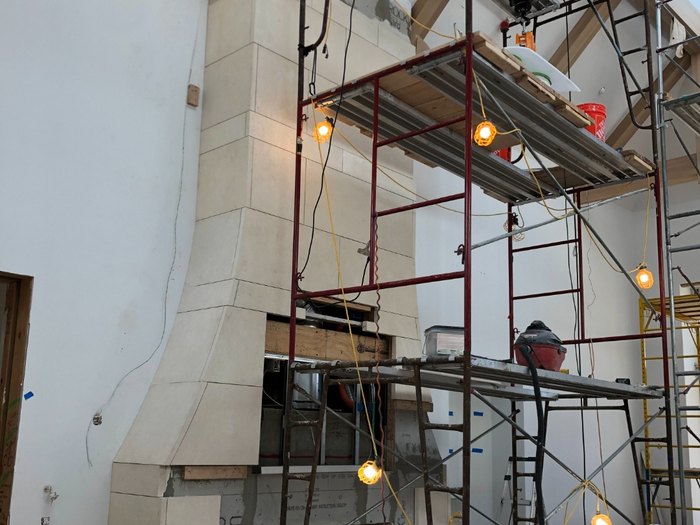 Cut limestone surround stacked to the ridge — flared base, tight joints, set off scaffold.