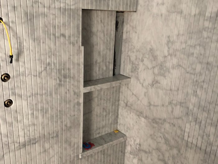 Shower wall in book-matched marble slab against fluted marble trim, with the niche cut in.