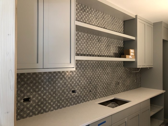 Patterned mosaic backsplash run full height behind floating shelves in the pantry.