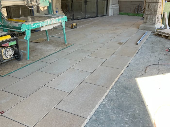 Terrace field going in off the wet saw — pavers set tight to the stone while the adjacent slab stays exposed.