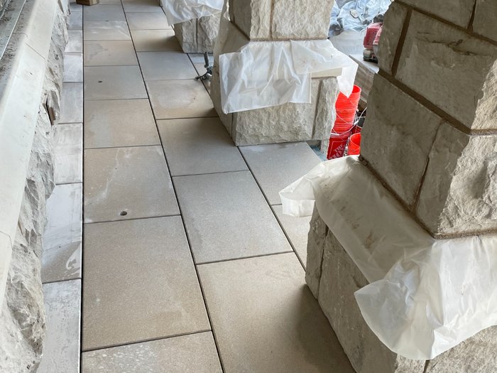 Narrow walkway threaded between the stone piers, stonework masked off while the pavers land.